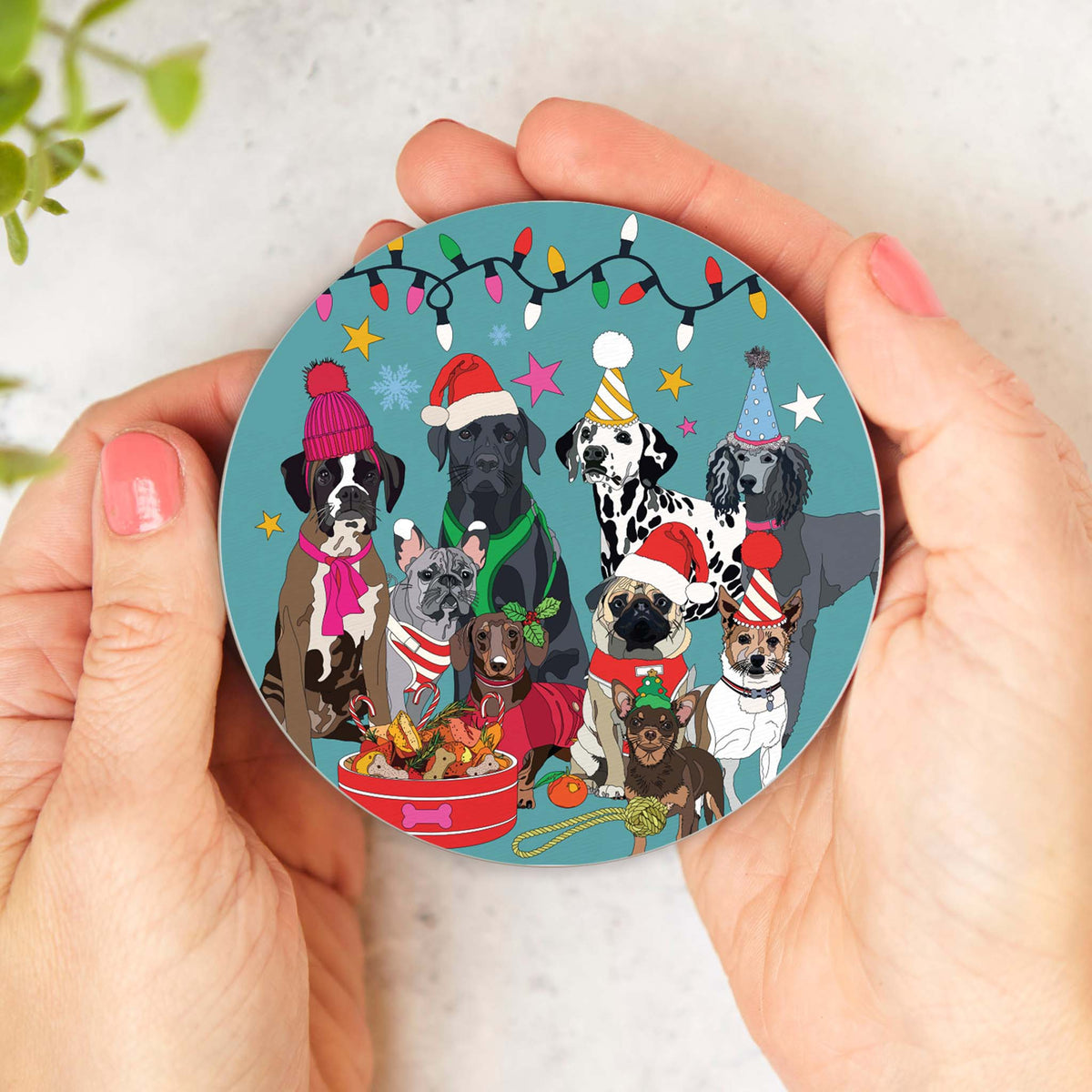 Round cork-backed coaster held in hands, featuring illustrated winter dogs in hats