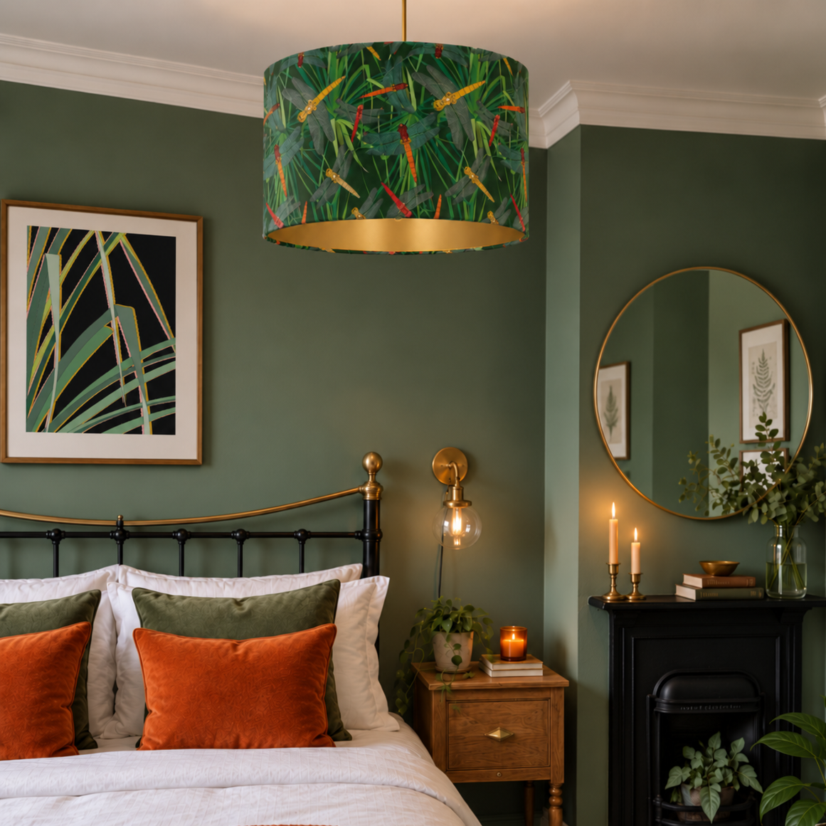 A styled bedroom interior featuring a green patterned drum pendant lamp with a gold interior, hanging above a bed with orange and green pillows in a dark green room.