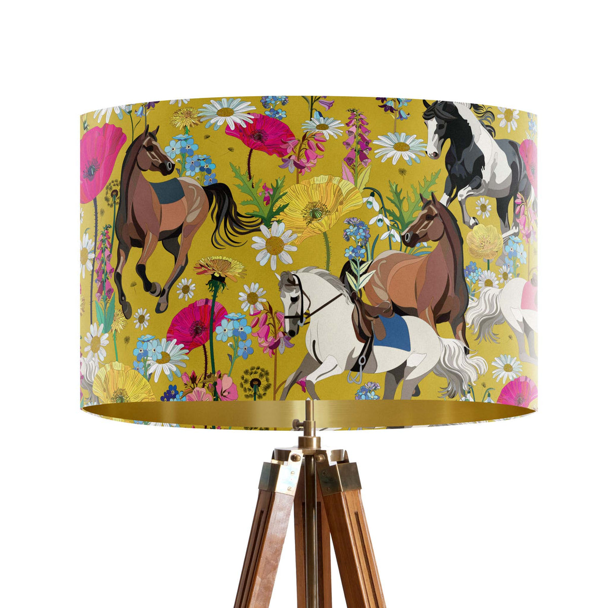 A table lamp with a large drum shade featuring a colorful pattern of horses and wildflowers on a mustard yellow background, supported by a wooden tripod base with brass hardware, shown on a plain white background.