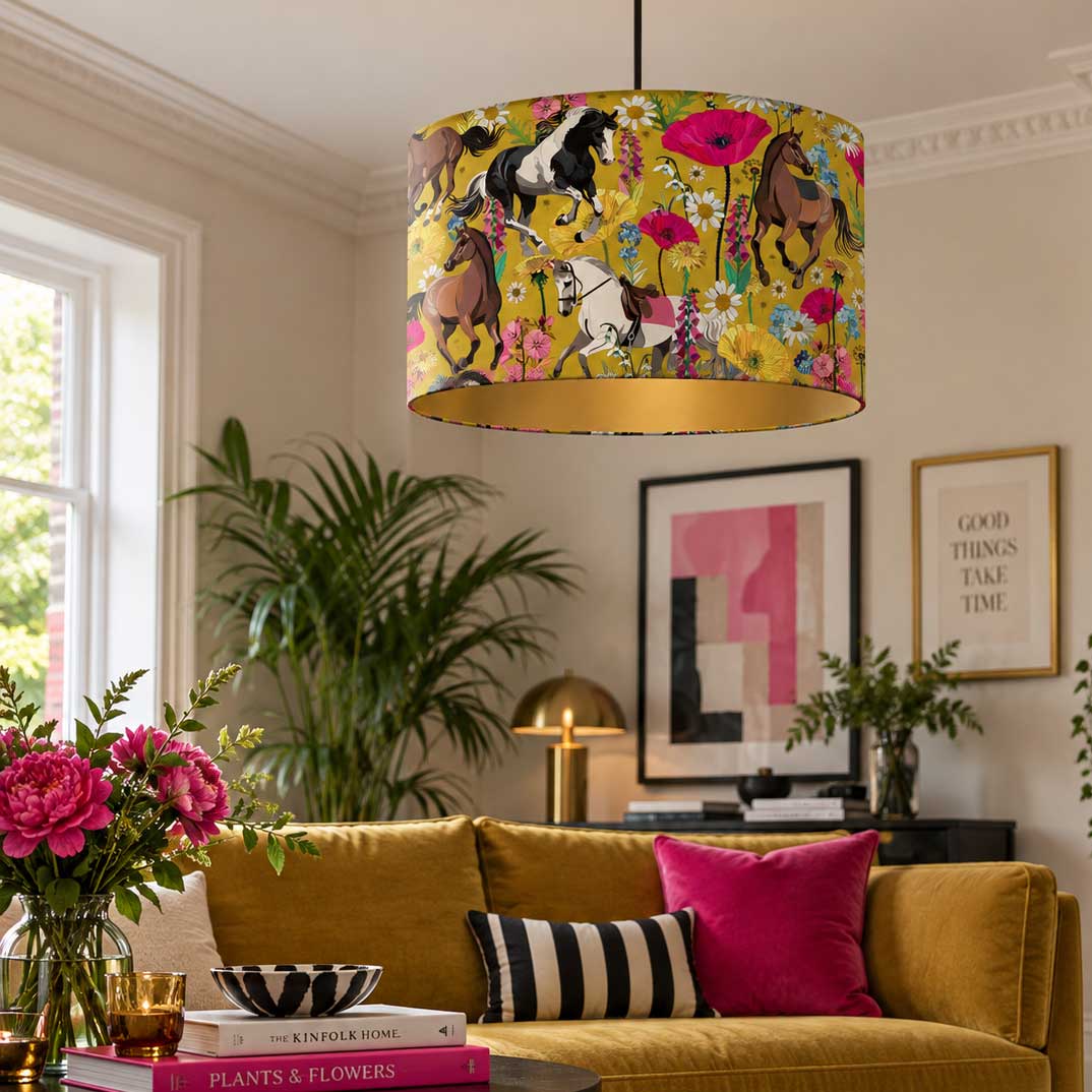 A drum pendant light with a vibrant yellow fabric shade featuring a whimsical print of horses, flowers, and butterflies, hanging in a styled living room above a mustard yellow sofa.
