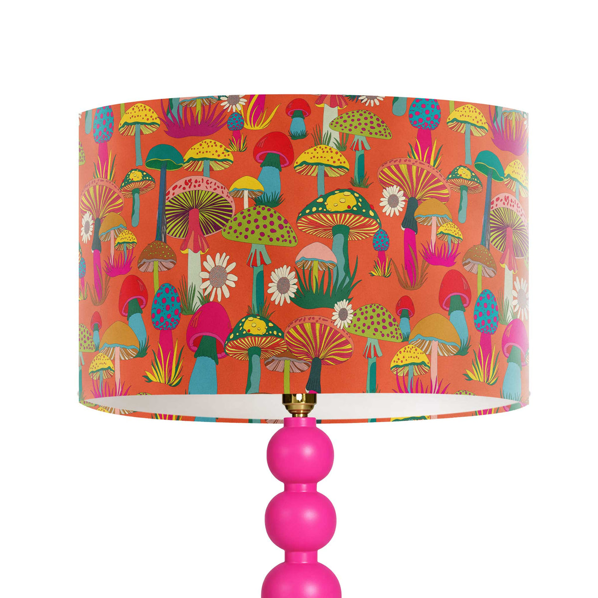 A table lamp with a bright pink multi-bulb base and a drum shade featuring a colorful retro mushroom pattern on an orange background.