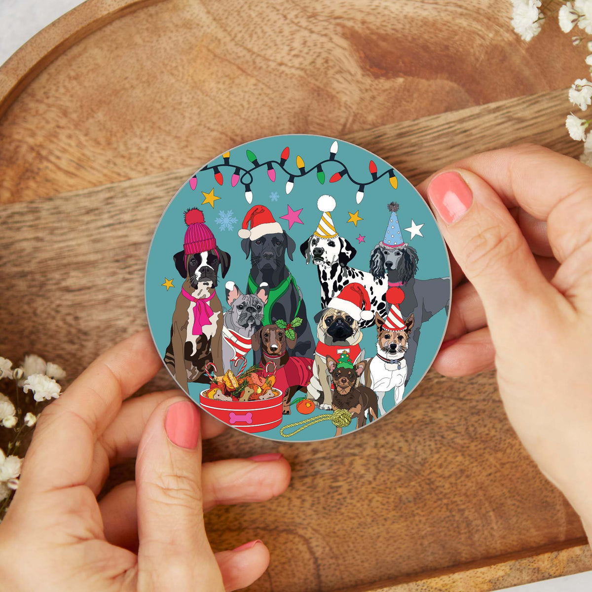Round cork-backed coaster held over a wooden surface, illustrated winter dogs