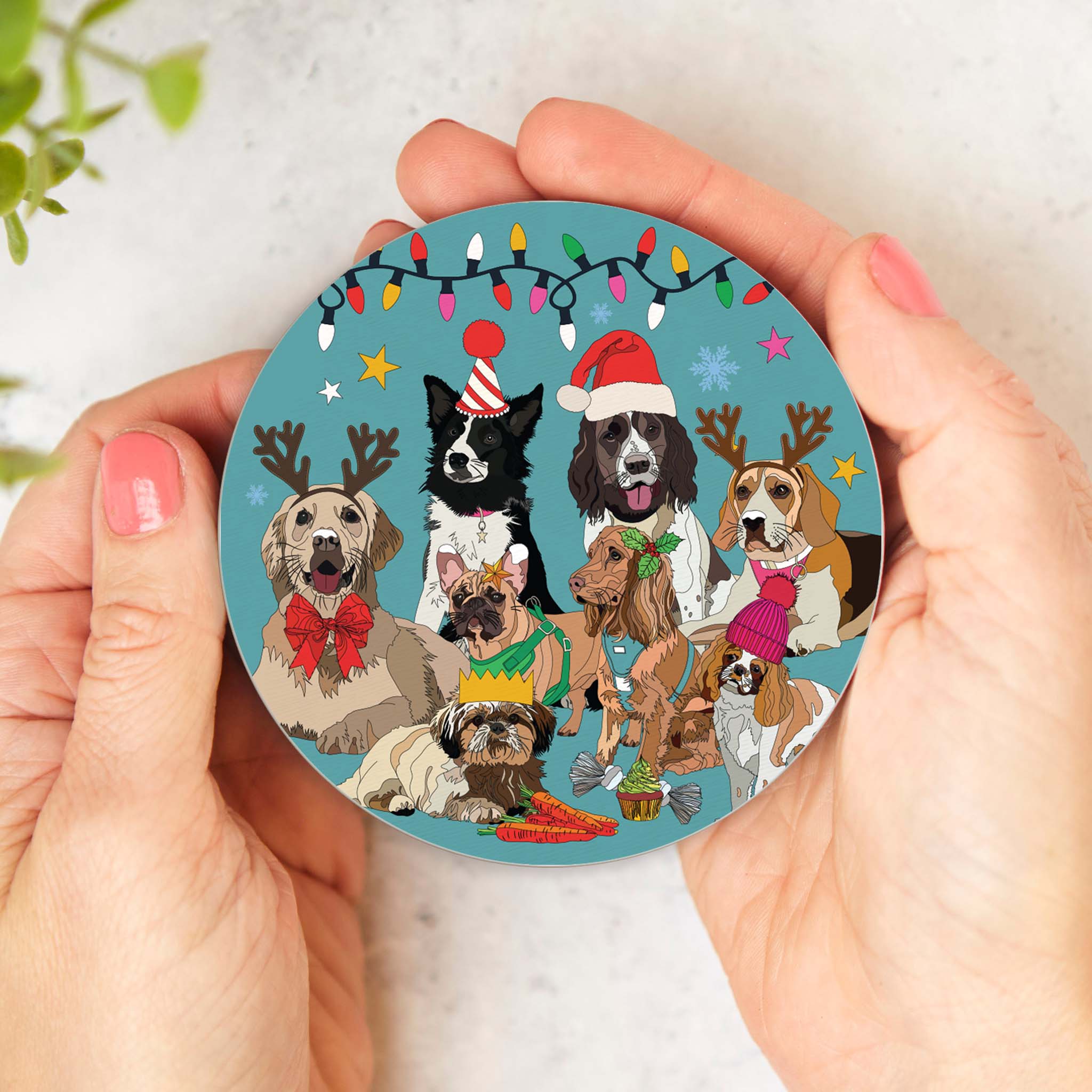 Round cork-backed coaster held in hands, featuring illustrated winter dogs with hats