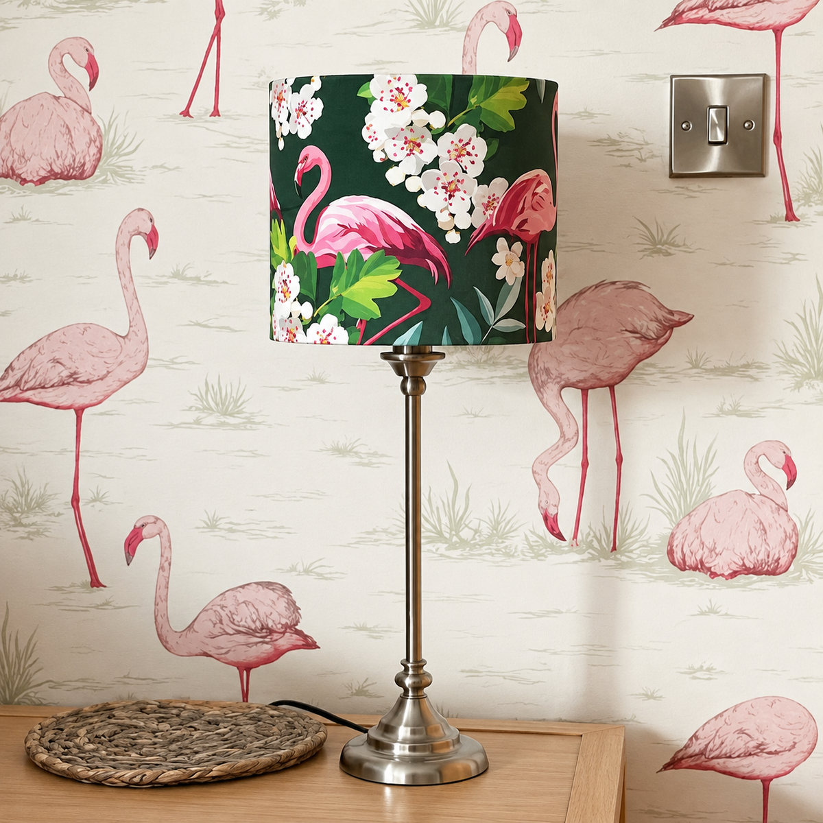 Flamingo velvet table lampshade with pink birds and white blossom on a dark green background, styled on a brass lamp base against pale flamingo wallpaper.