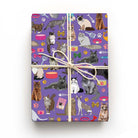 Whiskers purple cat wrapping paper on a wrapped gift, featuring illustrated Siamese, Persian, Bengal, tabby and long-haired cats.