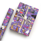 Purple cat patterned gift wrap with wrapped present and roll, featuring colourful cats, paw prints, collars, bows and fish bones.