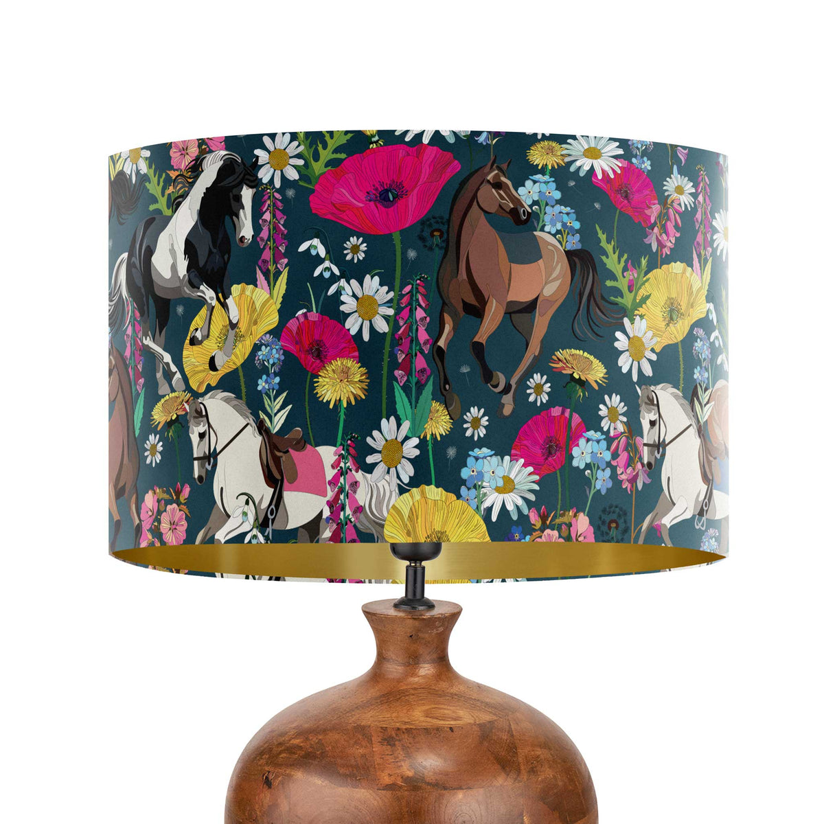 A table lamp with a dark teal drum shade featuring a colorful pattern of horses and wildflowers, set on a rustic brown ceramic base against a white background.