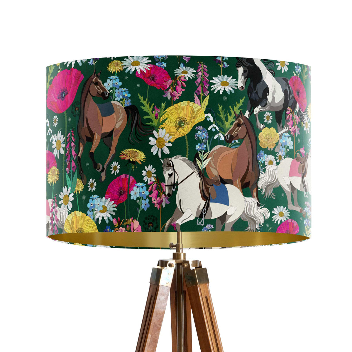 A tripod floor lamp with a dark green drum shade featuring a colorful pattern of horses and wildflowers, with a gold inner rim and a wooden tripod base.