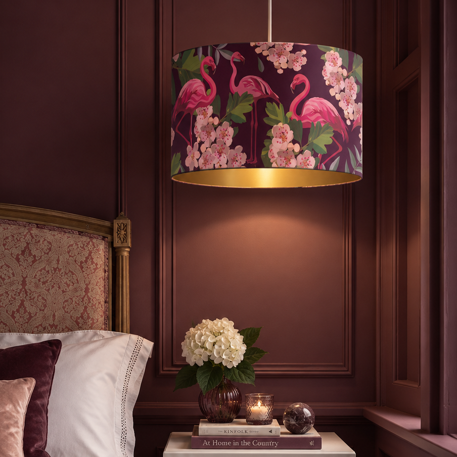 A drum pendant light with a pink flamingo and cherry blossom pattern hanging in a dark wood-paneled bedroom above a bedside table.