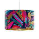 A drum pendant lamp shade featuring a vibrant, multicolored abstract floral pattern with a metallic gold inner rim, suspended by a thin white cord against a plain white background.