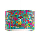 A drum pendant lamp shade featuring a vibrant, multicolored mushroom forest pattern on a turquoise blue background, suspended by a white cord against a plain white studio backdrop.