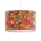 A drum-shaped pendant lampshade featuring a vibrant, multicolored retro mushroom pattern on a bright orange background, suspended by a thin white cord against a plain white wall.