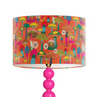A table lamp with a bright pink multi-bulb base and a drum shade featuring a colorful retro mushroom pattern on an orange background.