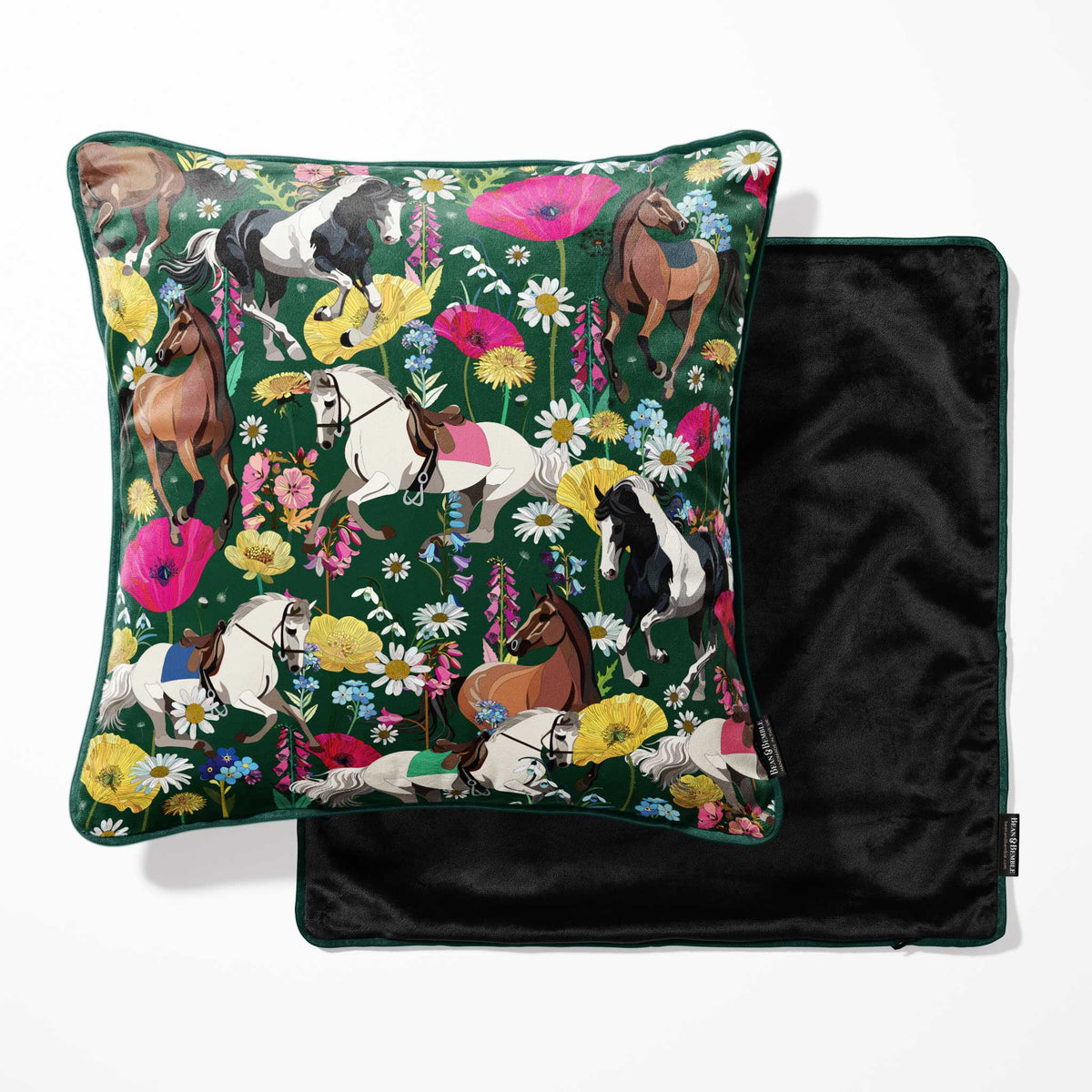 A square decorative pillow with a dark green background and an all-over equestrian floral print, shown with its black velvet reverse side partially visible behind it on a white background.