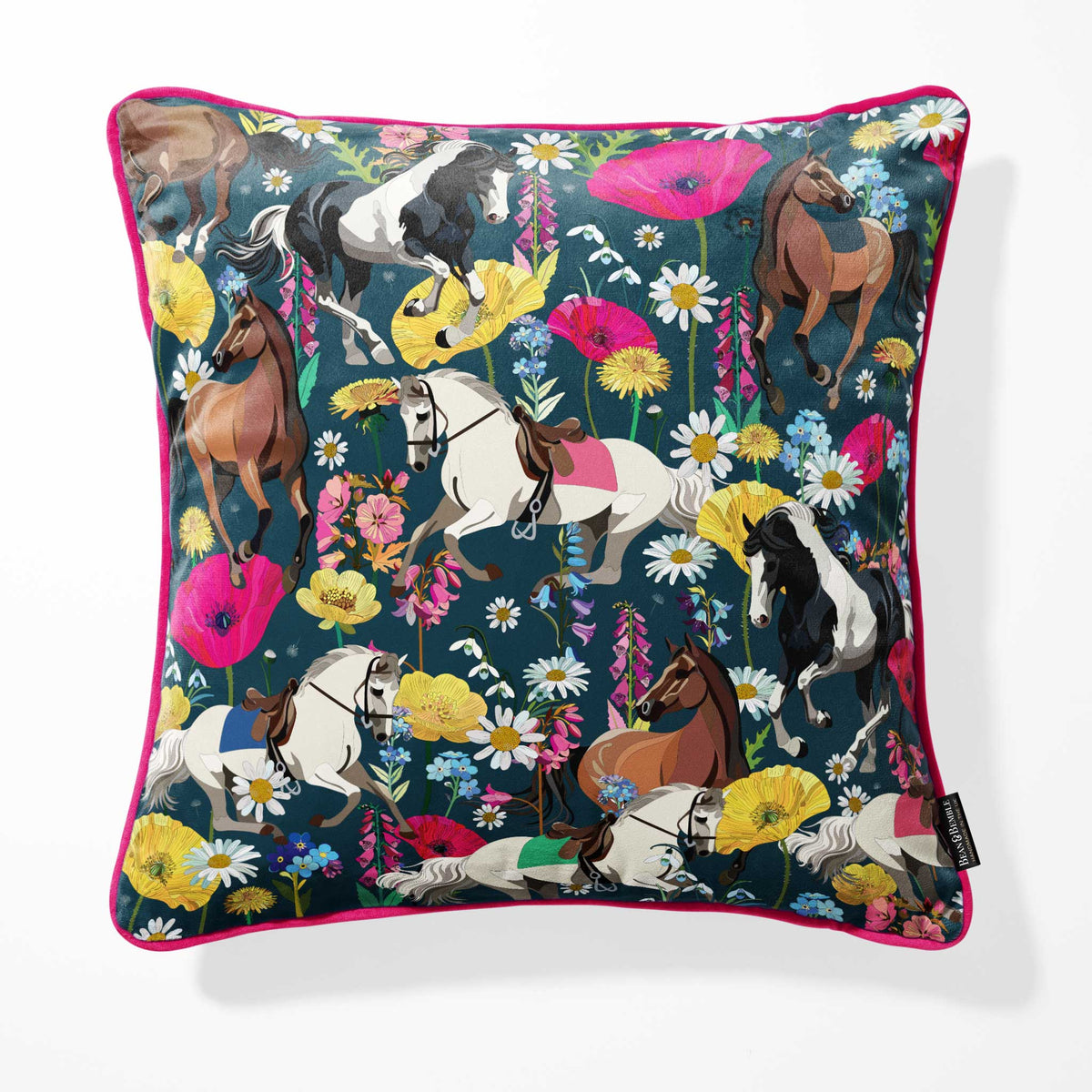 A square throw pillow featuring a vibrant, detailed print of horses, poppies, and wildflowers on a dark teal navy blue background, finished with a bright pink piped edge.