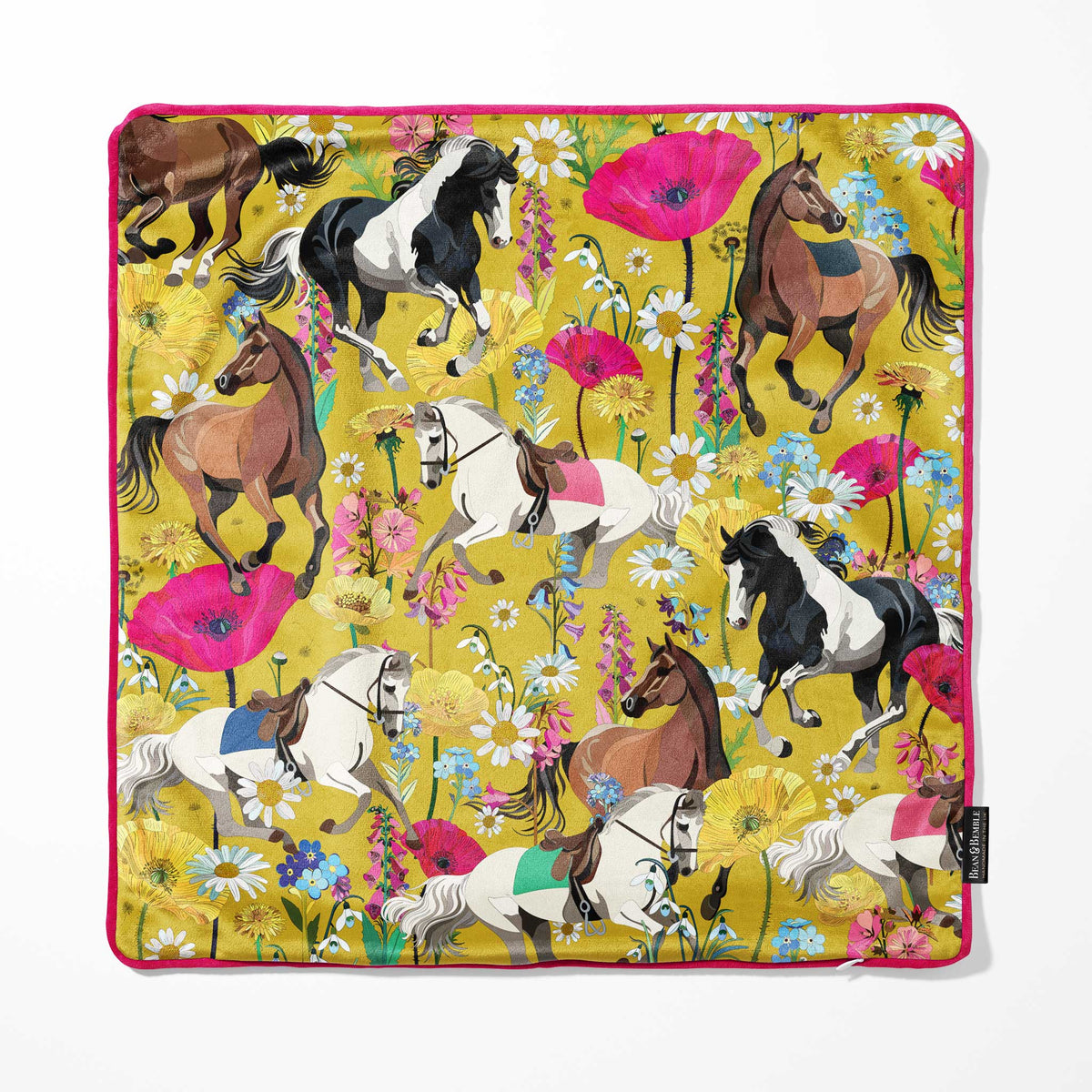 A square cushion cover with a vibrant yellow background, featuring an all-over print of horses in various breeds and colours, surrounded by colourful wildflowers. The cushion cover has bright pink piping and a small black Bean and Bemble brand tag on the bottom right edge.